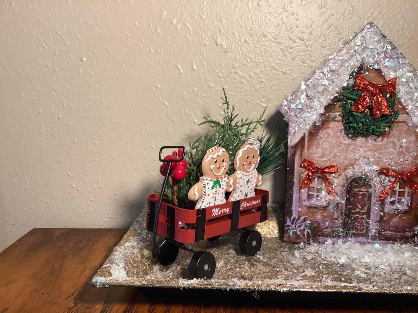 Adorable table top snow-covered gingerbread house with gingerbread cookies in a wagon, gold Christmas tree