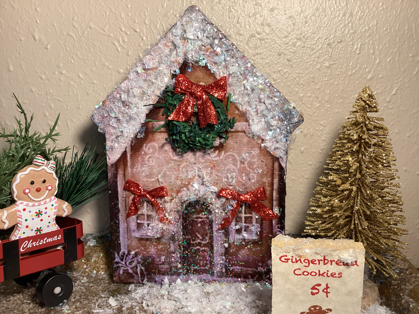 Adorable table top snow-covered gingerbread house with gingerbread cookies in a wagon, gold Christmas tree